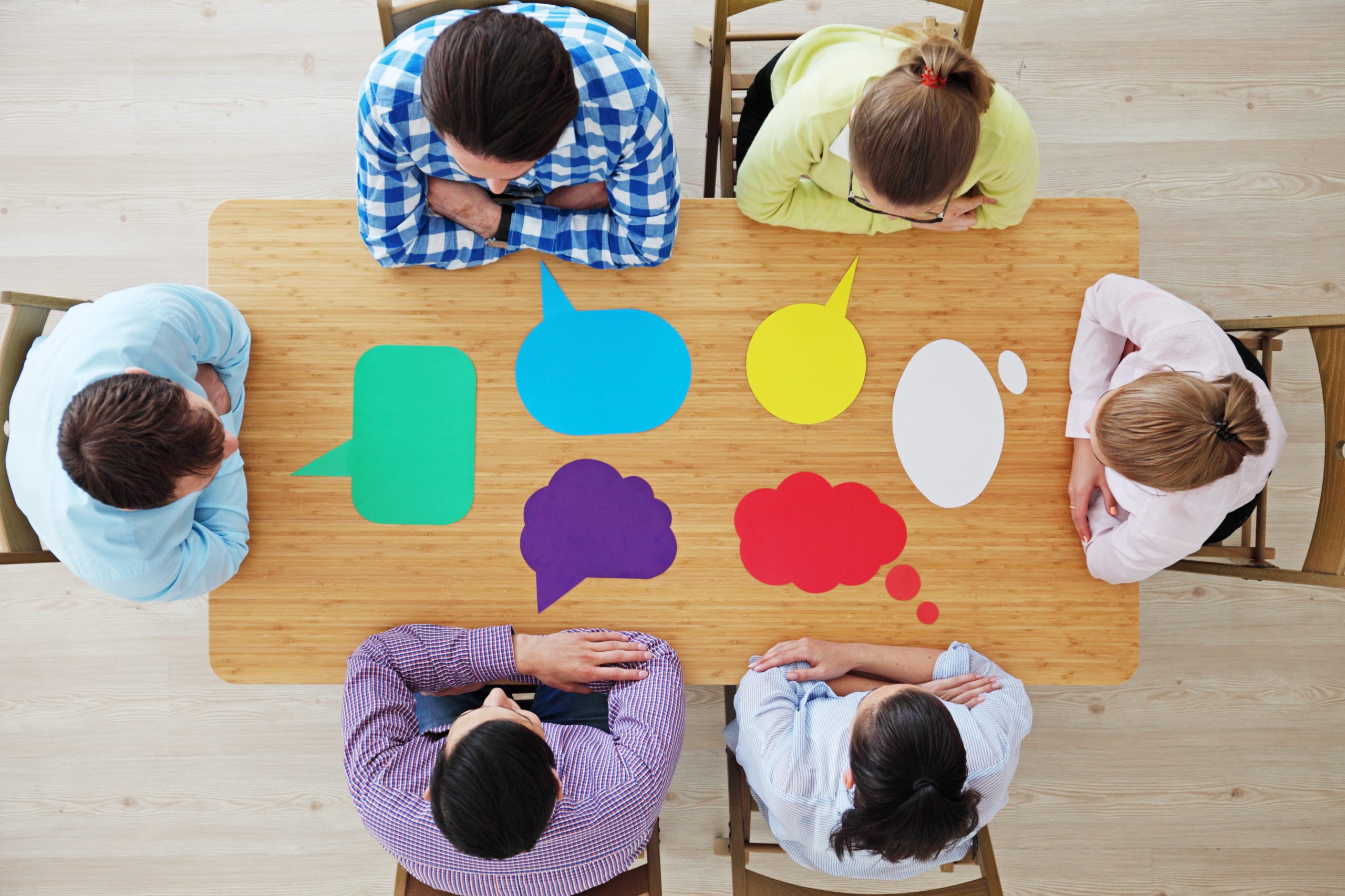 Team of business people in casual clothes sitting around the table with paper dialog boxes, discussing opinion concept